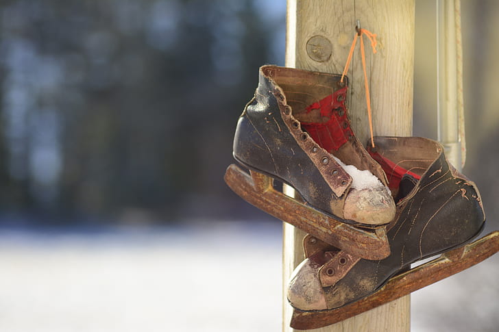 old black-and-brown ice skates hanging on gray wooden post during daytime