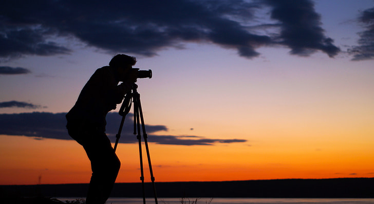 slihouette photo of man using telescope during sunset