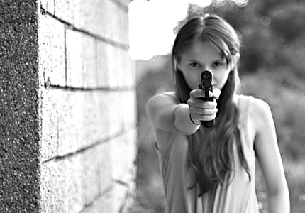 photo of woman wearing sleeveless top pointing gun near concrete wall