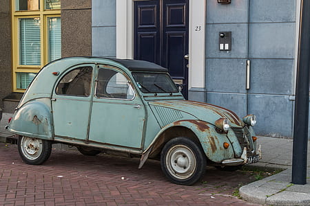 teal Volkswagen Type 1 parked beside blue and gray concrete building at daytime