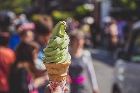 person's hand holding green icecream with cone
