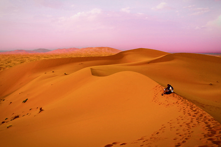 Two people sit in the sandy desert in Morocco, Africa
