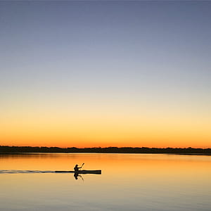 Silhouette of Man Inside of Boat Sailing on Body of Water during Sunset