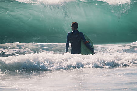 man in blue wet suit carrying a surf board