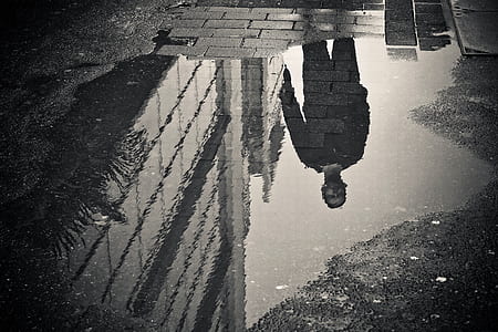 grayscale photo of man refletion on water