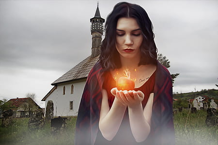 woman wearing red top and holding apple with fire during daytime