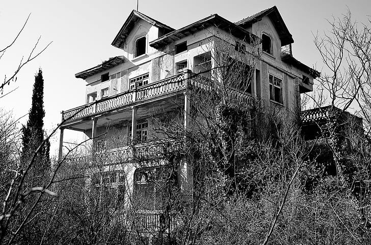 grayscale photography of 3-storey house near trees