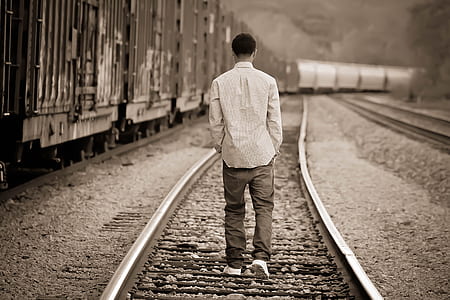 grayscale photo of man walking on train railway