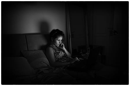 grayscale photograph of woman lying on bed using laptop