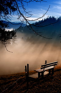 gray wooden bench on top of the mountain range overlooking the fog
