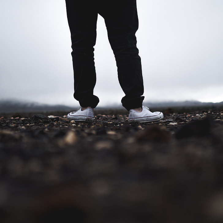 person in black pants wearing white Converse low top sneakers in tilt shift photography