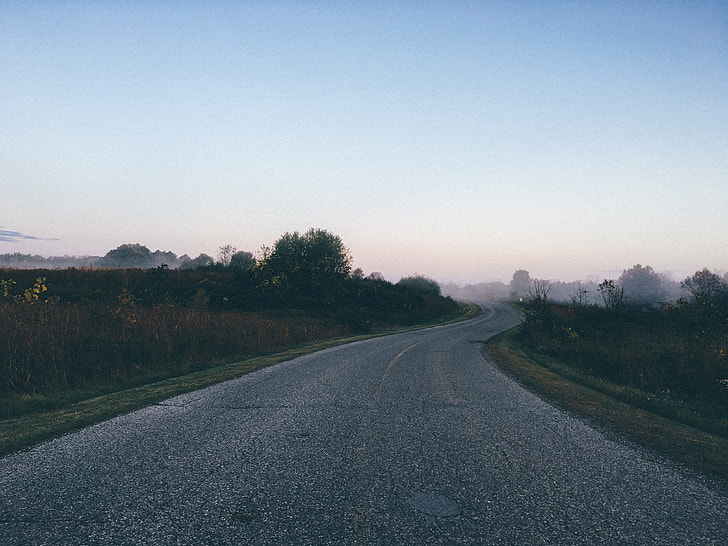 gray Asphalt road between green grass during dusk