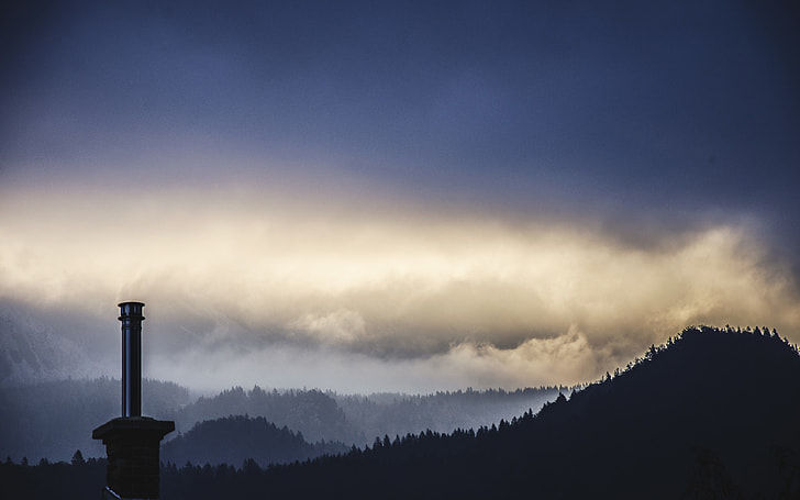 silhouette of light tower and mountain during cloudy day