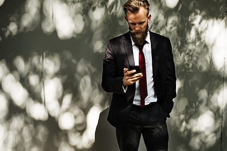 photo of man wearing black suit jacket with dress pants and white dress shirt holding phone