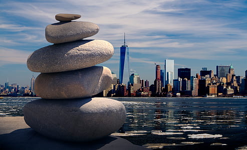 pile of stone near body of water with One World Trade Center building on background under cloudy sky at daytime