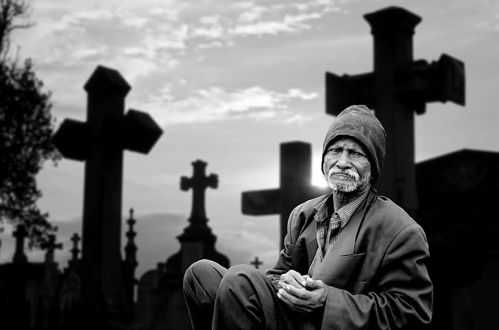 grayscale photo of a man sitting near black cross