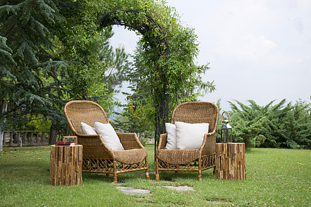 two brown wicker armchairs with white throw pillows beside two round tables on grass field