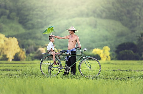 man wearing black pants standing beside green city bicycle with boy wearing white button-up shirt