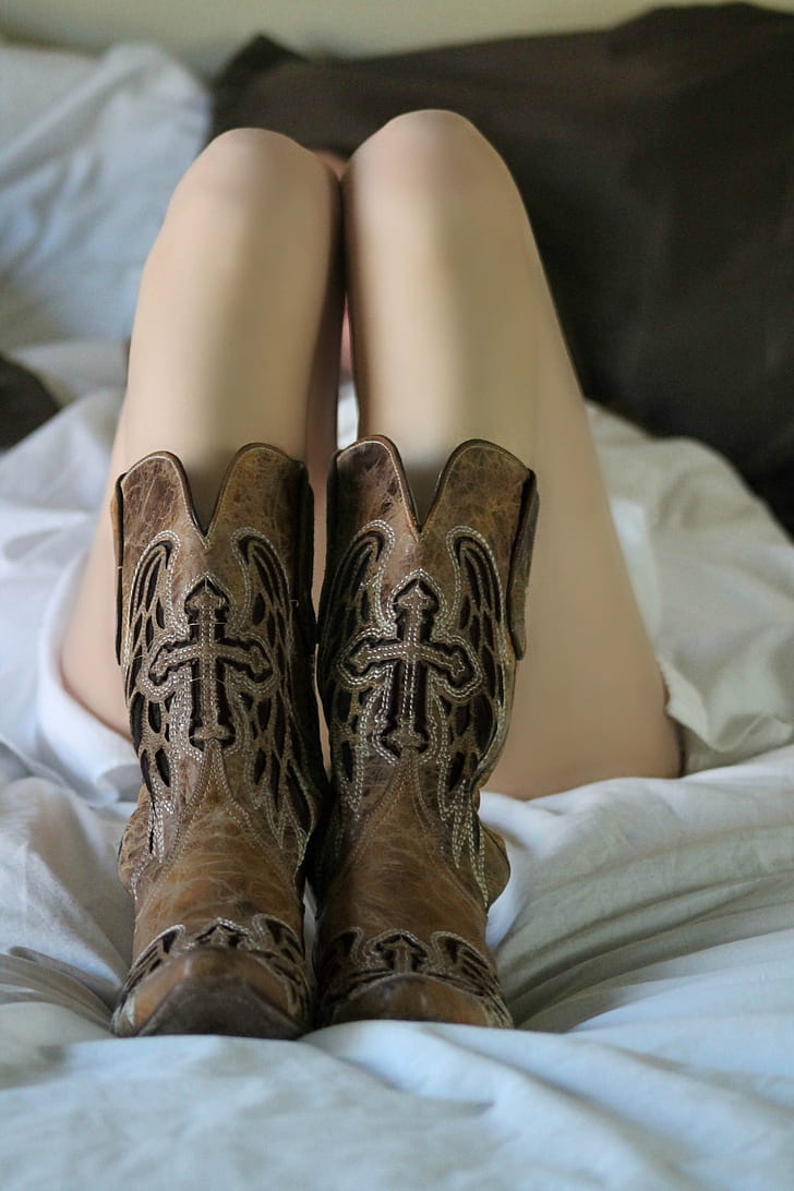 person wearing brown leather x-toe cowboy boots lying on bed