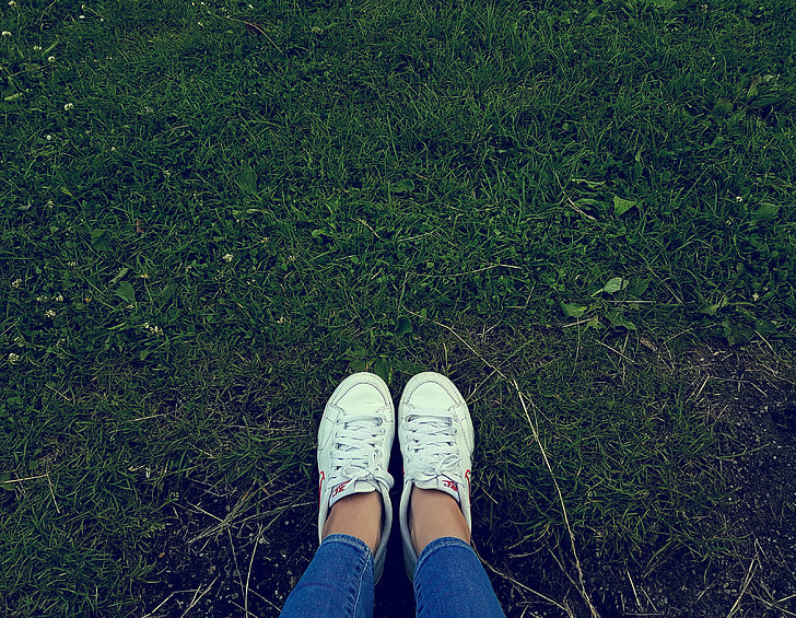 person wearing white low-top sneakers  standing on green grass
