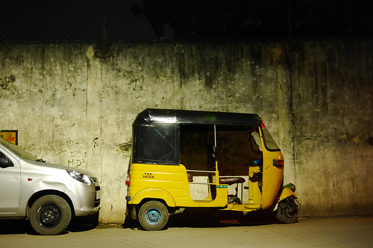 yellow and black auto rickshaw parked by gray concrete wall