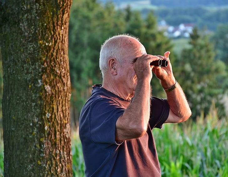 man wearing gray t-shirt near tree using black binoculars