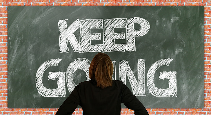 person standing in front of green chalkboard with Keep Going text