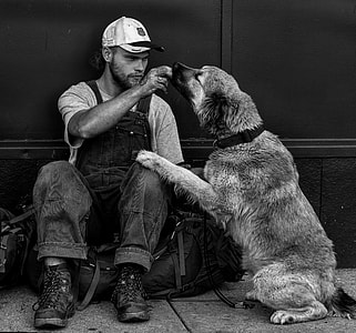 grayscale photography of man in dungaree sitting beside dog