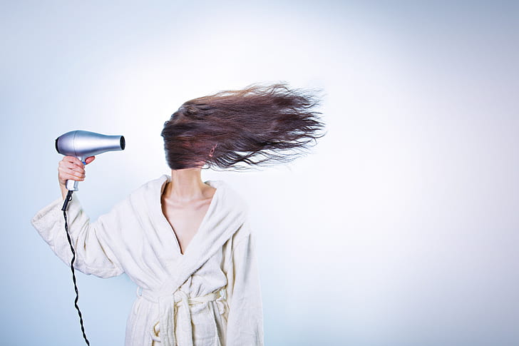 woman holding hair blower performing to dry her hair