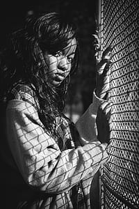 Grey Scale Photography of Woman Standing Against Mesh Grill