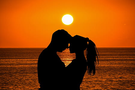 man and woman hugging by the beach with ocean on the horizon during sunset