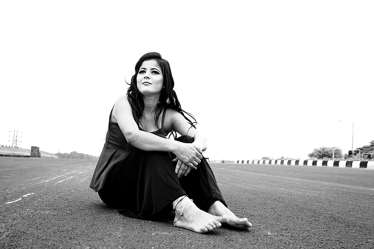 grayscale photo of woman sitting on road