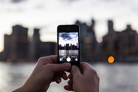 A person captures the sunset over the Manhattan skyline in New York with their iPhone mobile smartphone. Image taken from DUMBO, Brooklyn