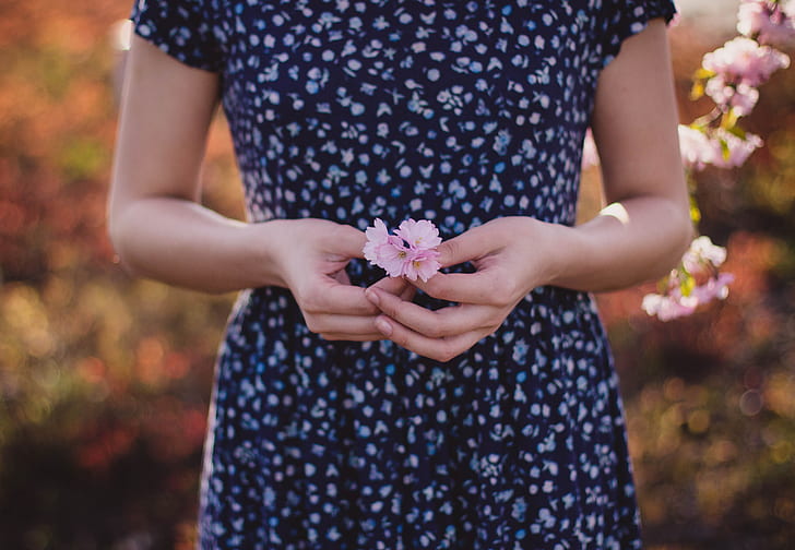 woman in blue short-sleeved dress holding pink flowers in shallow photograpy