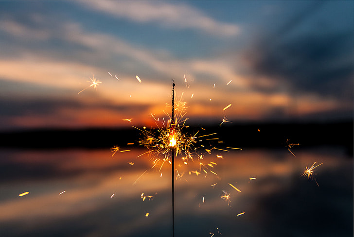 selective focus photography of sparkler firework under blue and white sky