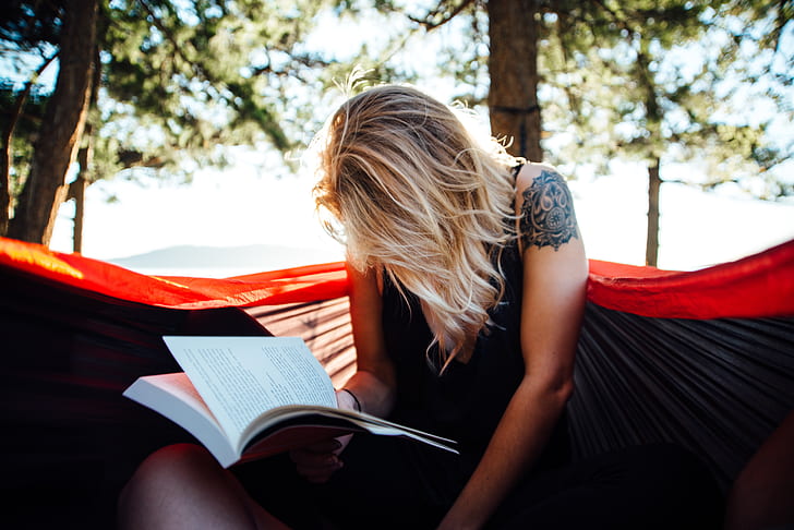 woman reading book on hammock at daytime