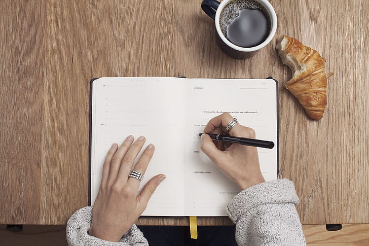 woman in sweater writing on her planner wallpaper