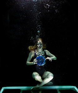woman underwater holding analog twin bell clock at 10:10