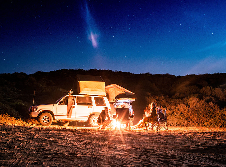 people camping beside white car during night time