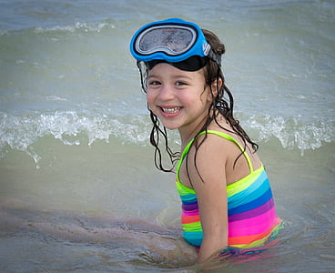 girl wearing multicolored striped top and blue swimming goggles on body of watr