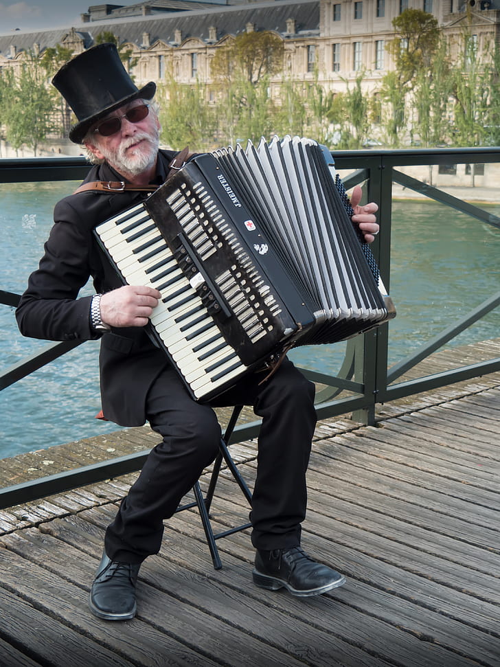 man playing accordion near body of water during daytime