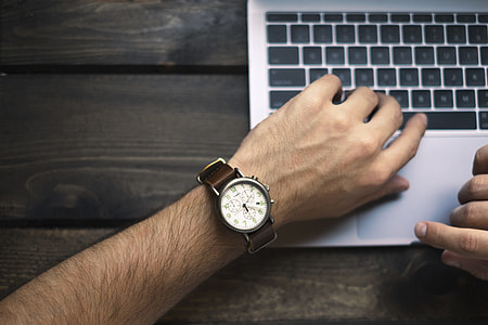 man in white analog watch holding silver laptop computer