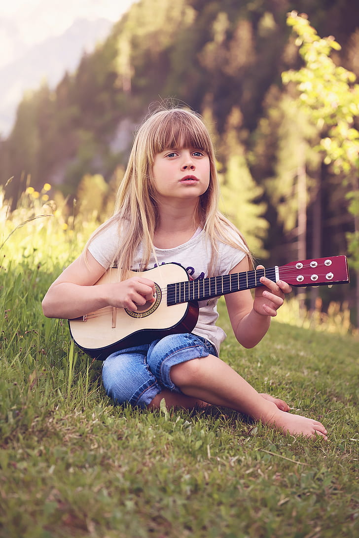 girl in white t-shirt playing beige and brown guitar on grass field during daytime