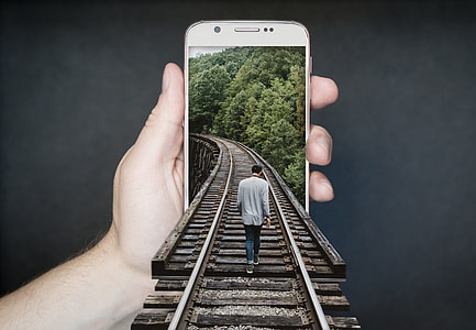 man walking on train rail through person holding white smartphone optical illusion artwork