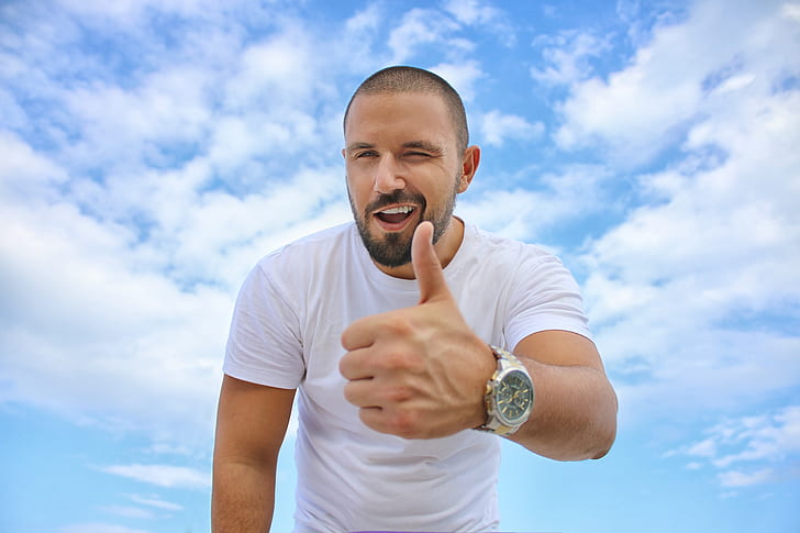 man wearing white shirt doing thumbs up under cumulus clouds