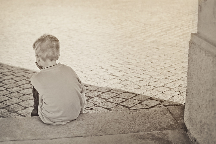 boy wearing gray top sitting on gray concrete surface