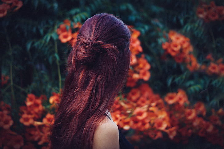 woman with red hair facing away towards red flowers