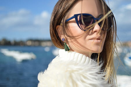 selective focus photography of woman wearing blue framed black lens sunglasses and white fur-lined coat