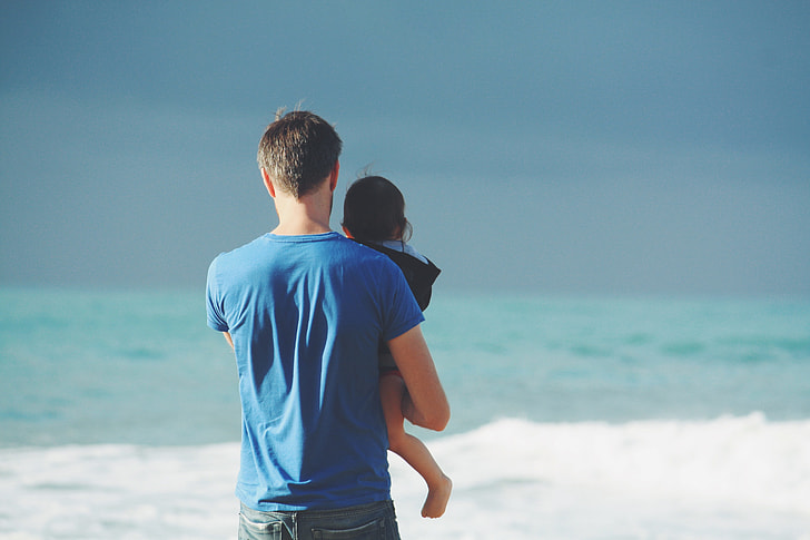man in blue shirt carrying baby beside seashore
