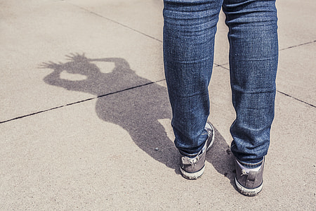 person's shadow wearing blue jeans and pair of gray sneakers